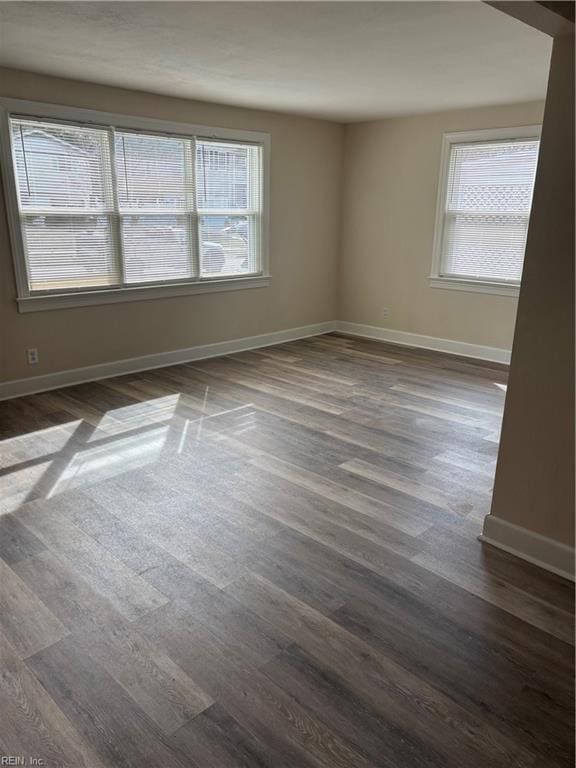 empty room with dark wood-style floors, a healthy amount of sunlight, and baseboards