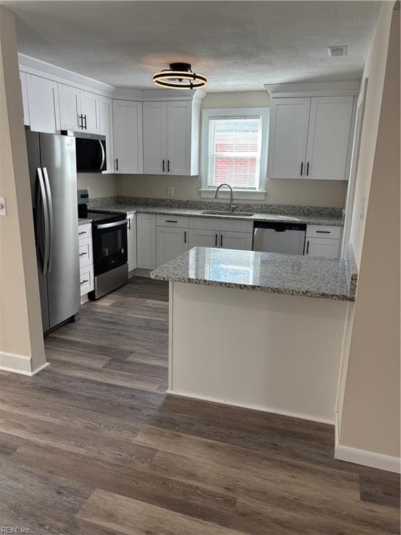 kitchen with light stone countertops, appliances with stainless steel finishes, dark wood-style floors, white cabinetry, and a sink