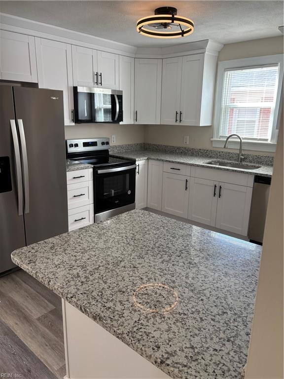 kitchen with dark wood finished floors, appliances with stainless steel finishes, light stone countertops, and a sink