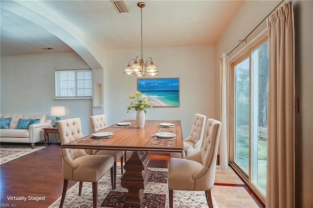 dining area featuring visible vents, arched walkways, an inviting chandelier, and wood finished floors