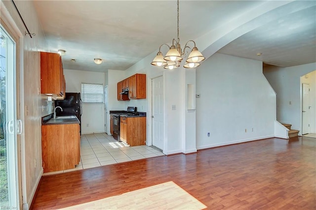 kitchen with brown cabinets, a sink, dark countertops, gas stove, and light wood finished floors