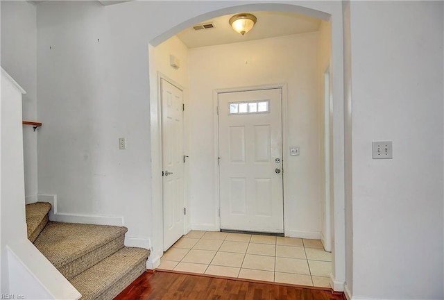 foyer with visible vents, baseboards, stairs, light tile patterned floors, and arched walkways