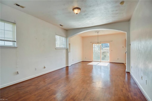 spare room with visible vents, arched walkways, baseboards, and wood finished floors