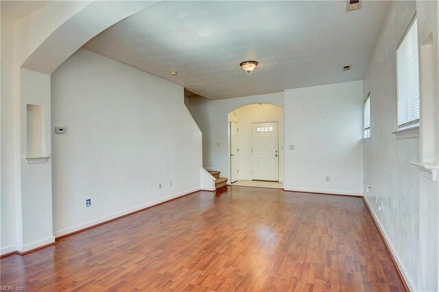 empty room with arched walkways, stairs, baseboards, and wood finished floors