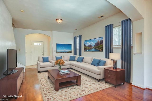 living area with wood finished floors, visible vents, and arched walkways