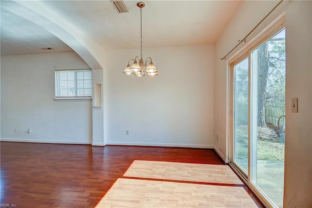 empty room with visible vents, baseboards, dark wood finished floors, arched walkways, and a notable chandelier