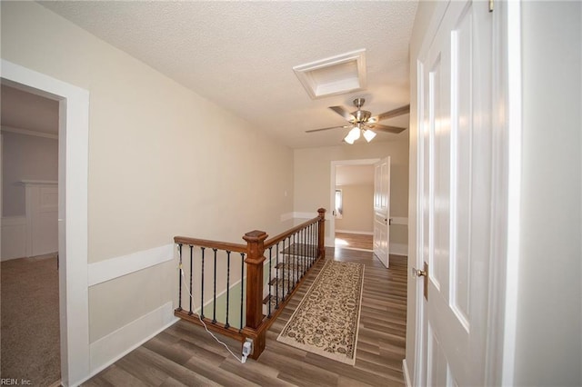 corridor featuring a wainscoted wall, an upstairs landing, a textured ceiling, and wood finished floors