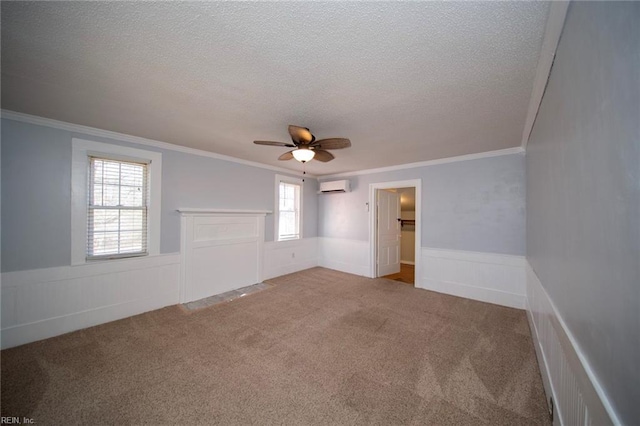 carpeted spare room featuring an AC wall unit, a textured ceiling, wainscoting, crown molding, and ceiling fan