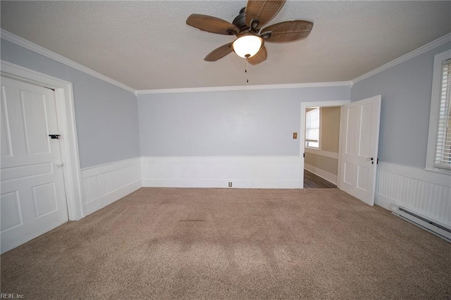 carpeted spare room with wainscoting, a baseboard heating unit, a textured ceiling, and crown molding