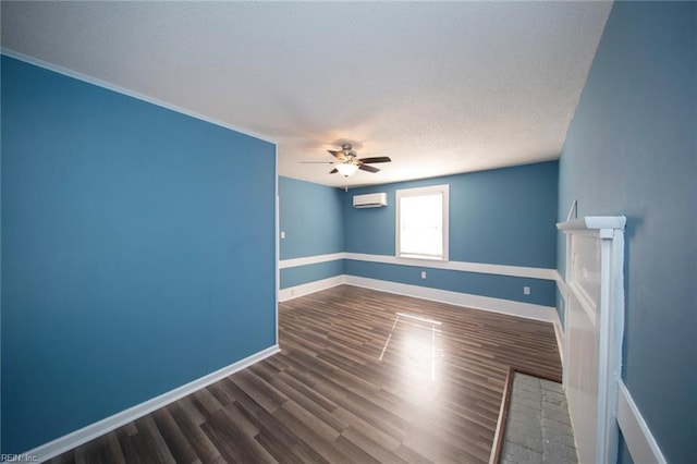 empty room with a wall mounted AC, a textured ceiling, wood finished floors, baseboards, and ceiling fan