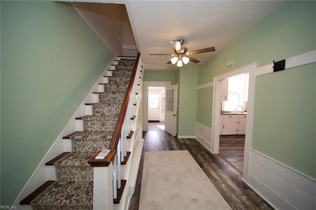 stairway with wainscoting, a textured ceiling, ceiling fan, and wood finished floors