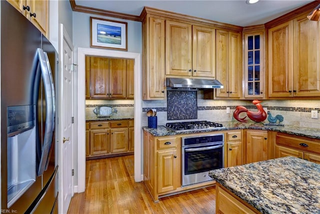 kitchen featuring under cabinet range hood, light wood finished floors, appliances with stainless steel finishes, and dark stone counters