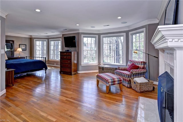 bedroom featuring wood finished floors, baseboards, a fireplace with flush hearth, recessed lighting, and crown molding