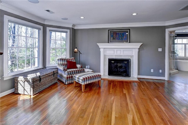 sitting room with a glass covered fireplace, wood finished floors, baseboards, and ornamental molding