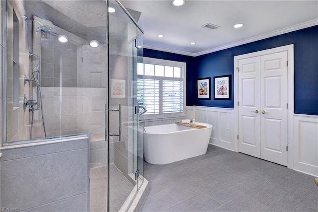 full bathroom featuring a wainscoted wall, visible vents, a freestanding tub, a stall shower, and crown molding