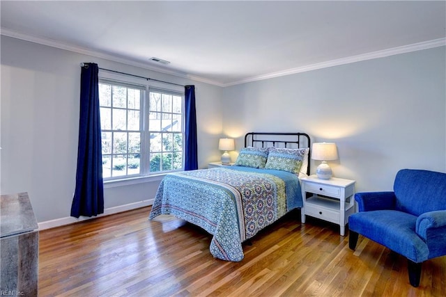 bedroom featuring visible vents, baseboards, wood finished floors, and ornamental molding