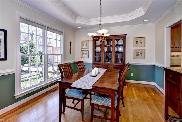 dining area featuring visible vents, ornamental molding, a tray ceiling, light wood-style floors, and baseboards