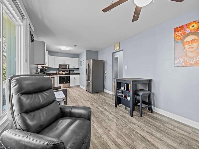 living room featuring baseboards, light wood-style floors, and a ceiling fan