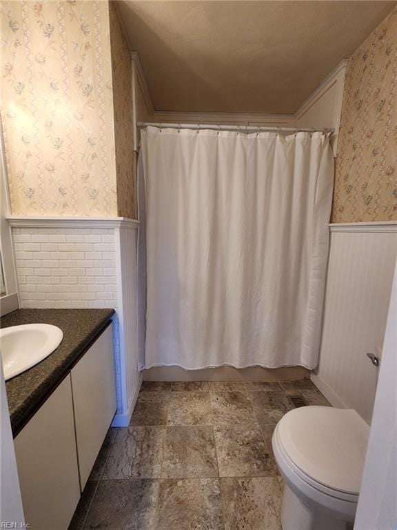 bathroom featuring toilet, shower / bath combo, wainscoting, wallpapered walls, and vanity