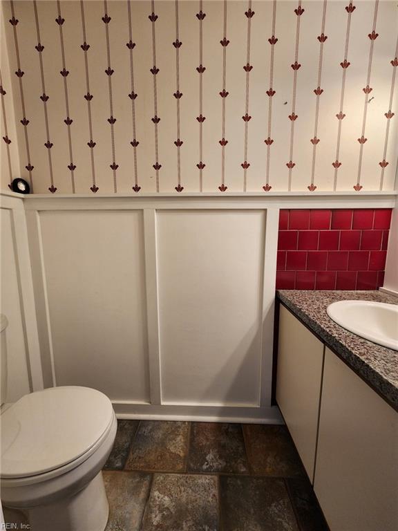 bathroom featuring stone tile floors, backsplash, toilet, and vanity