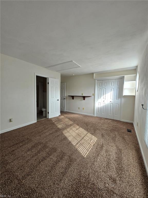 carpeted empty room featuring attic access and baseboards