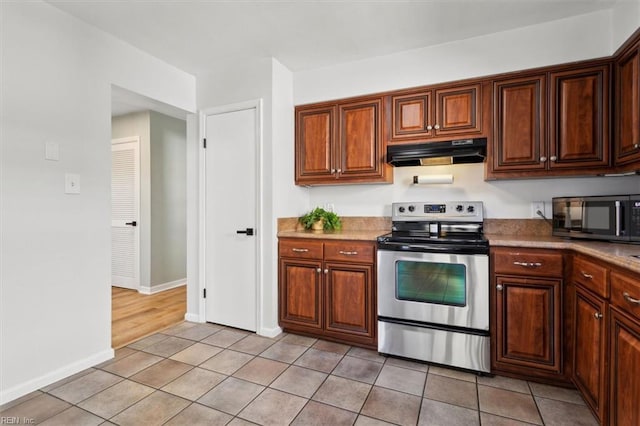 kitchen with under cabinet range hood, stainless steel electric range oven, baseboards, and light tile patterned floors