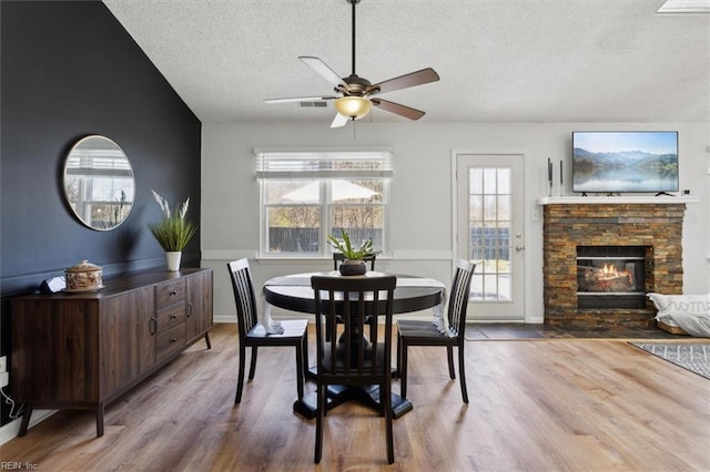 dining area featuring a fireplace, vaulted ceiling, wood finished floors, and a textured ceiling