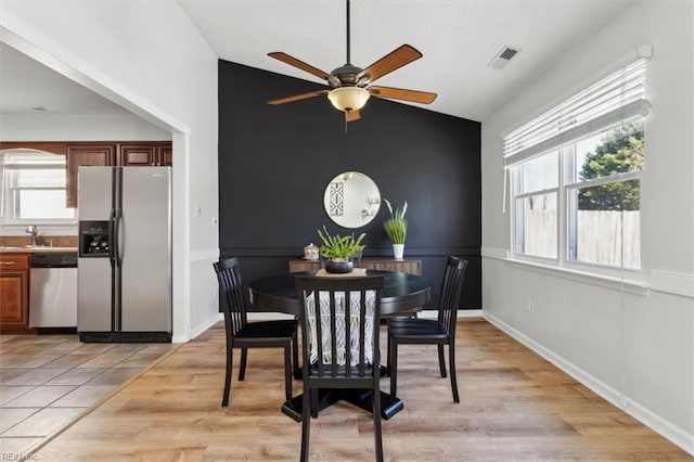 dining room featuring visible vents, light wood-style flooring, baseboards, lofted ceiling, and ceiling fan