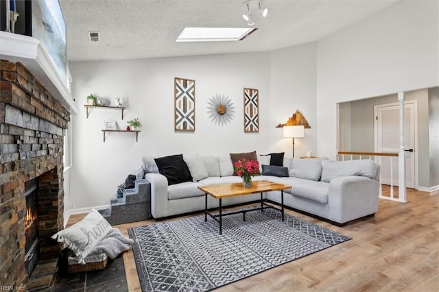 living area with wood finished floors, visible vents, a textured ceiling, lofted ceiling with skylight, and a brick fireplace