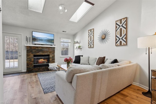 living area featuring vaulted ceiling with skylight, a fireplace, baseboards, and wood finished floors