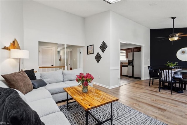 living area with a high ceiling, light wood finished floors, baseboards, ceiling fan, and ornate columns