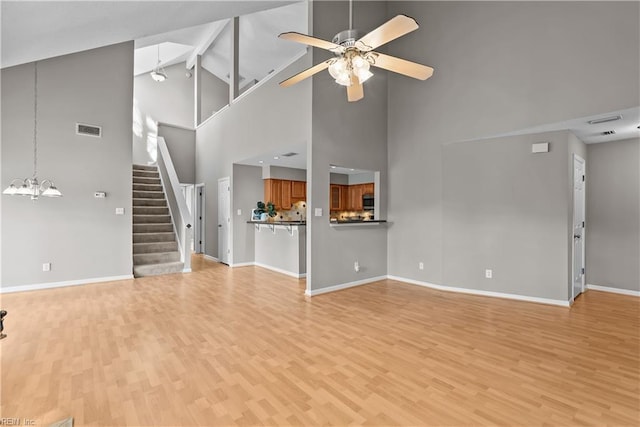 unfurnished living room featuring visible vents, ceiling fan with notable chandelier, light wood finished floors, baseboards, and stairs