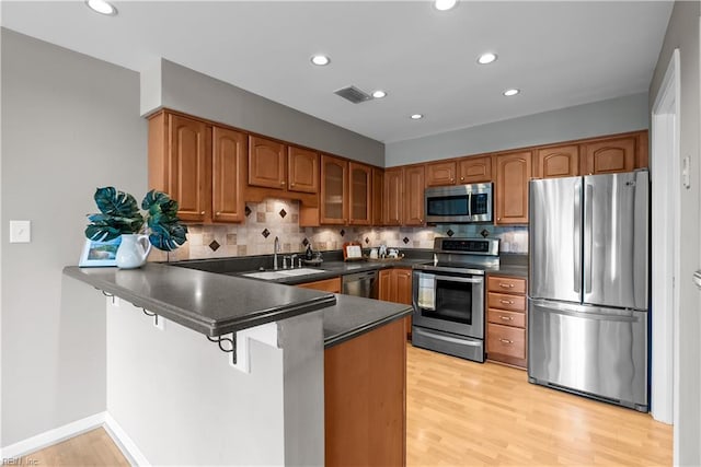 kitchen featuring a peninsula, a sink, appliances with stainless steel finishes, dark countertops, and brown cabinets