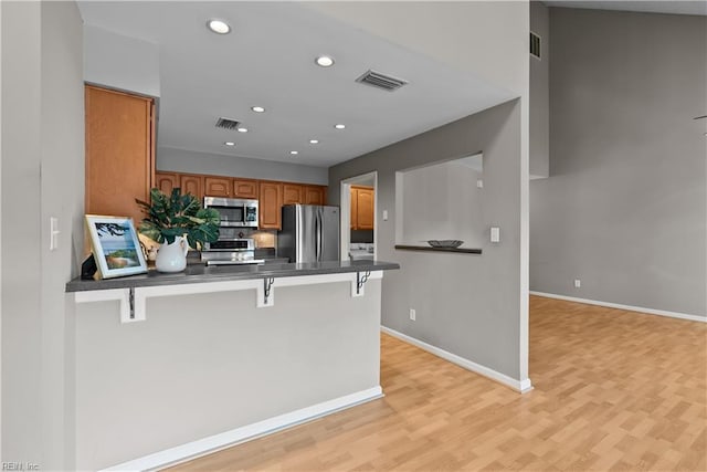 kitchen featuring visible vents, a peninsula, stainless steel appliances, dark countertops, and brown cabinets