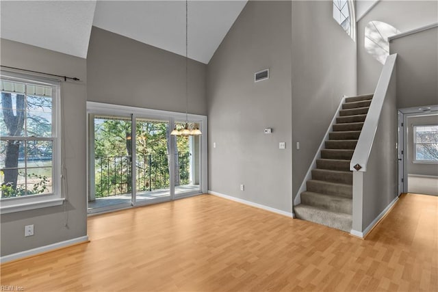 unfurnished living room featuring a chandelier, visible vents, stairway, and a wealth of natural light