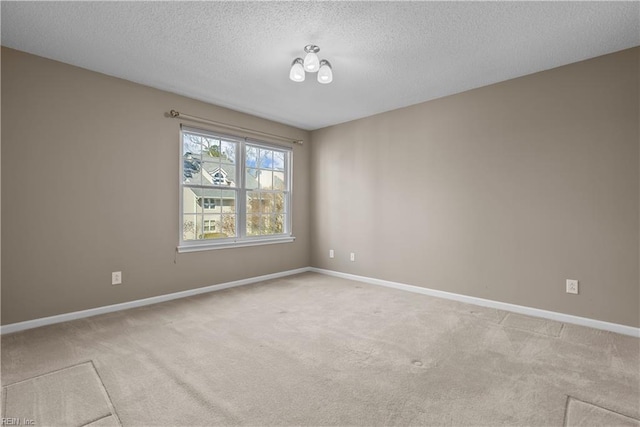 spare room with light colored carpet, a textured ceiling, and baseboards