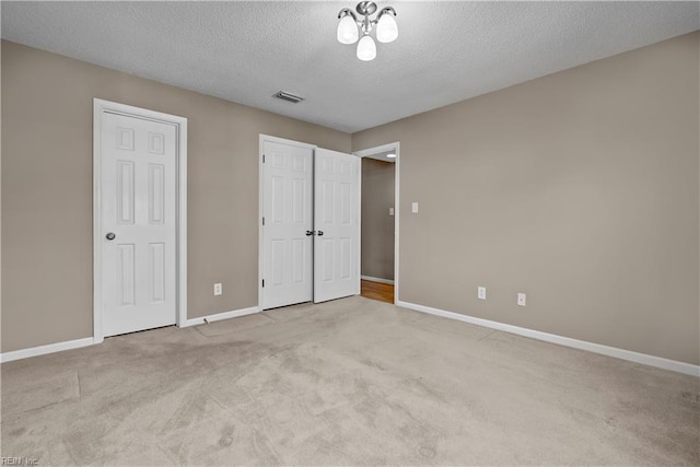 unfurnished bedroom featuring visible vents, multiple closets, a textured ceiling, carpet flooring, and baseboards