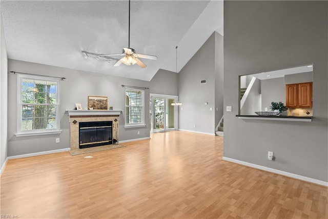 unfurnished living room with a tiled fireplace, stairway, a healthy amount of sunlight, and light wood-style flooring