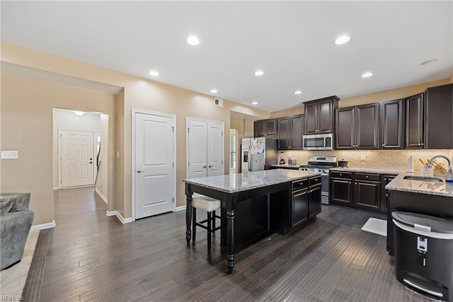 kitchen featuring a kitchen bar, a sink, tasteful backsplash, a center island, and appliances with stainless steel finishes