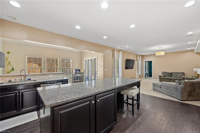 kitchen featuring a sink, open floor plan, recessed lighting, a breakfast bar area, and dark cabinets