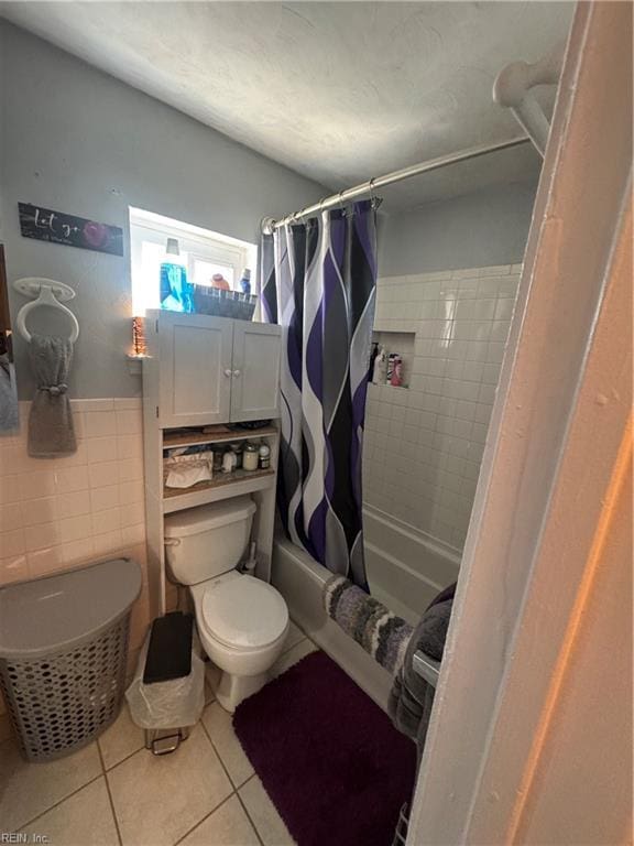 bathroom featuring toilet, shower / tub combo with curtain, tile walls, wainscoting, and tile patterned flooring