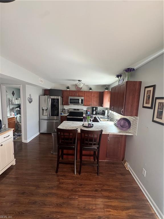 kitchen with a breakfast bar, dark wood finished floors, appliances with stainless steel finishes, a peninsula, and light countertops