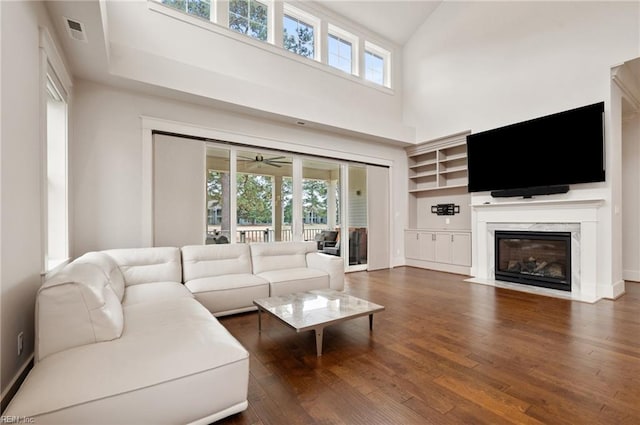 living room featuring visible vents, a premium fireplace, a high ceiling, wood finished floors, and a ceiling fan