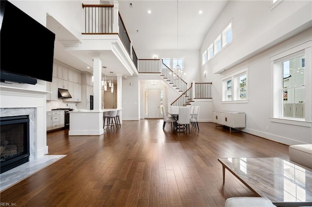 unfurnished living room with dark wood-type flooring, a high ceiling, a fireplace, baseboards, and stairs