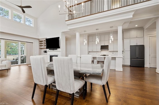 dining room featuring dark wood finished floors, ceiling fan with notable chandelier, a fireplace, and high vaulted ceiling