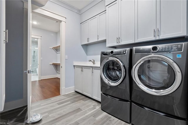 washroom with cabinet space, washing machine and dryer, light wood-type flooring, and baseboards