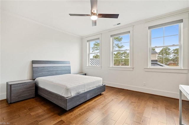 bedroom with wood finished floors, visible vents, baseboards, ceiling fan, and ornamental molding