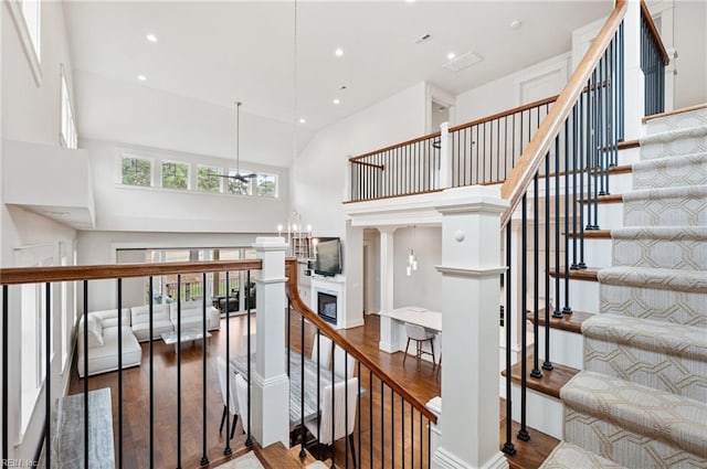 stairs with wood finished floors, recessed lighting, a towering ceiling, a glass covered fireplace, and a chandelier