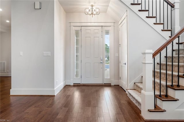 foyer entrance featuring visible vents, wood finished floors, stairway, an inviting chandelier, and baseboards