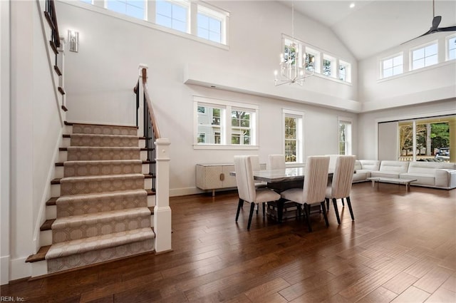 dining area featuring baseboards, a chandelier, stairway, wood finished floors, and high vaulted ceiling